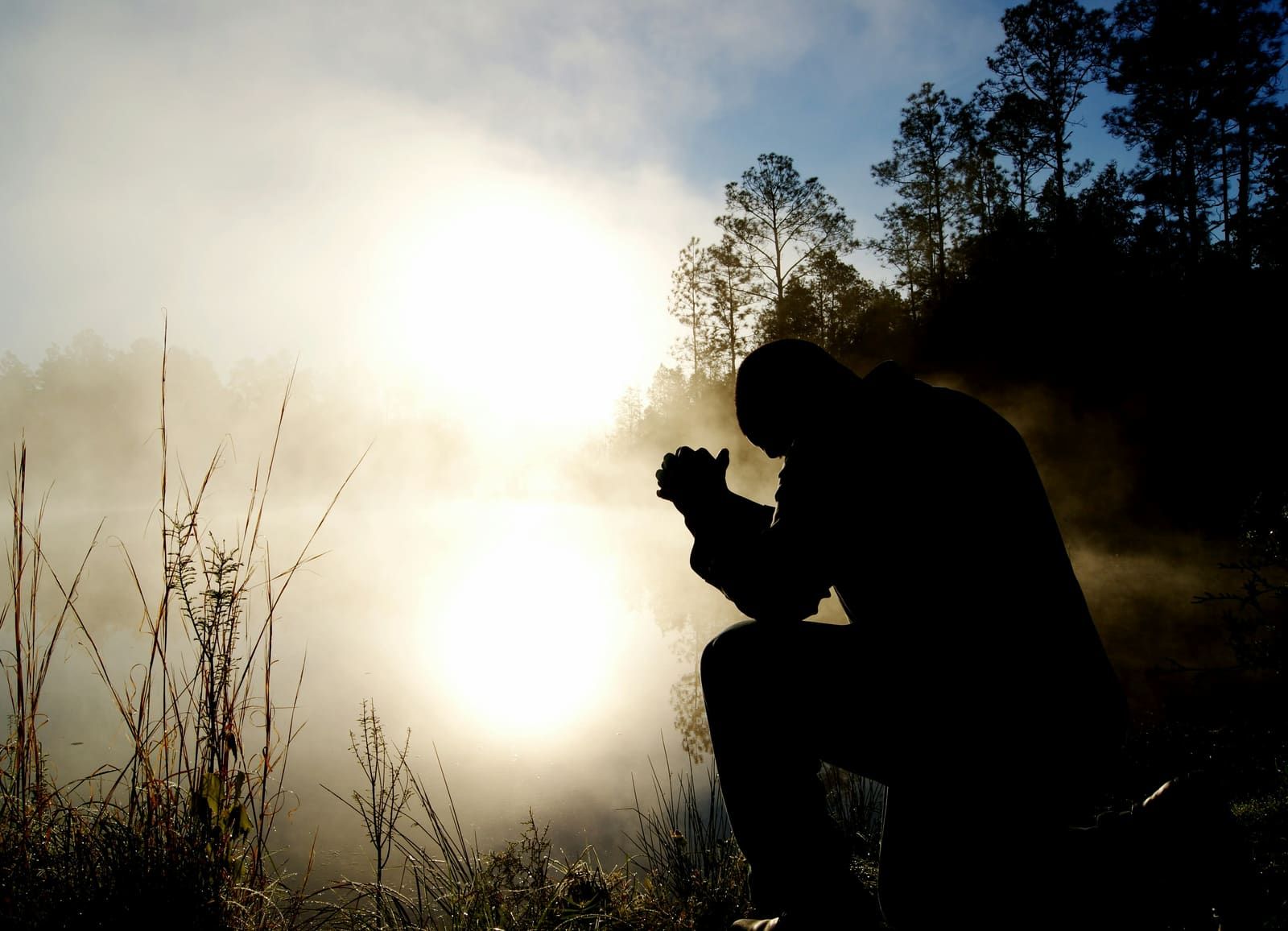 A silhouette praying at sunrise by a foggy lake