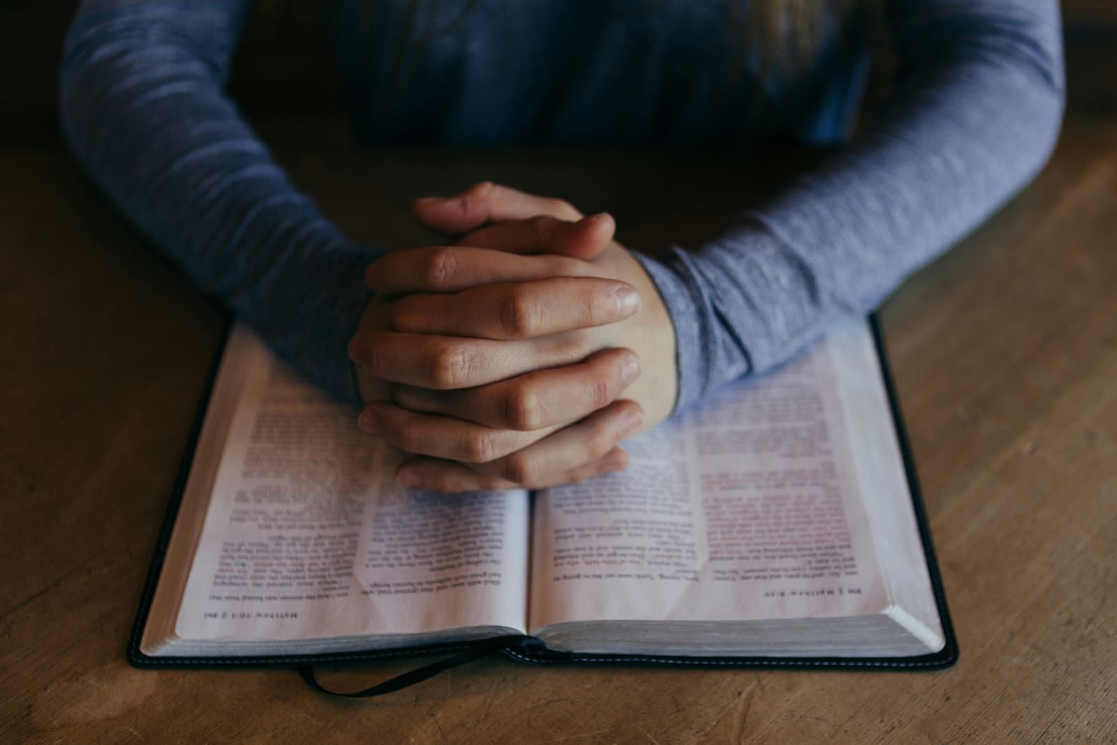 Hands clasped in prayer over an open Bible